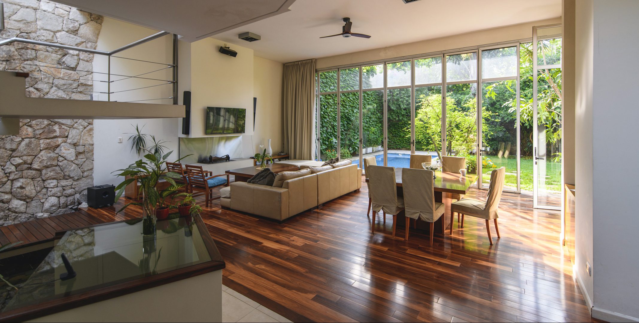 Wide angle perspective of naturally lit spacious modern home interior with full length windows and view of backyard and swimming pool.